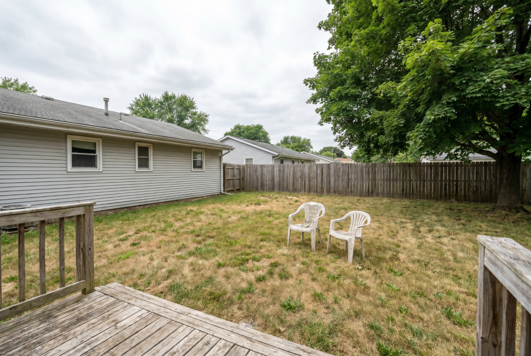 Frankfort backyard before, patchy lawn with two weathered white plastic chairs and a wood privacy fence